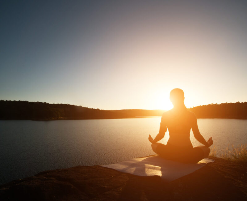 Silhouette of healthy woman is practicing yoga at mountain lake