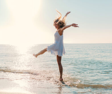 young attractive happy woman dancing turning around by sea beach sunny summer fashion style in white dress vacation