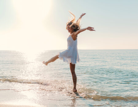 young attractive happy woman dancing turning around by sea beach sunny summer fashion style in white dress vacation